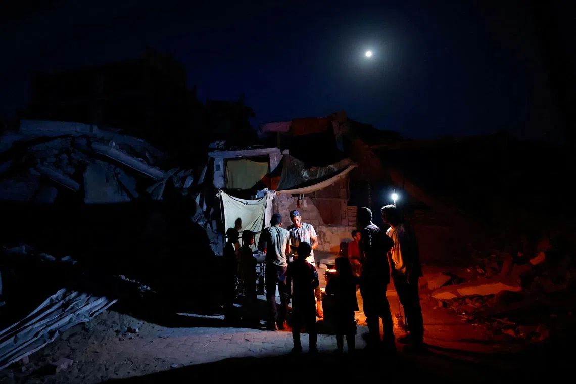 Palestinians gathering amid a power outage near houses destroyed during Israel's military offensive, in Khan Younis, in the southern Gaza Strip, on June 19, 2024. 