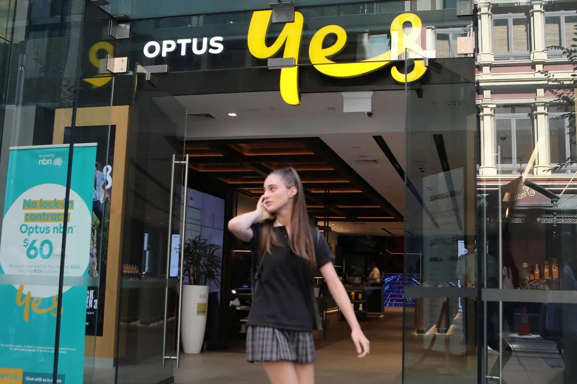 A woman uses her mobile phone as she walks past an Optus shop in Sydney in 2018.  Australia’s No. 2 telco on Wednesday reported a major outage across its mobile phone and Internet networks affecting millions of customers but the company did not specify if it was due to a cyber incident.