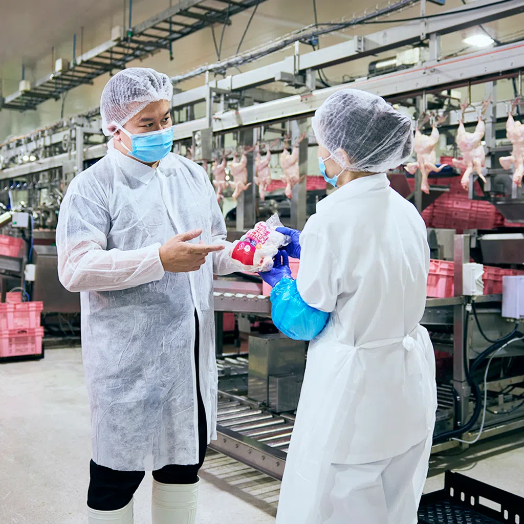 kee song corporate affairs officer james sim holding organic sakura chicken product and speaking with employee at the chicken processing floor