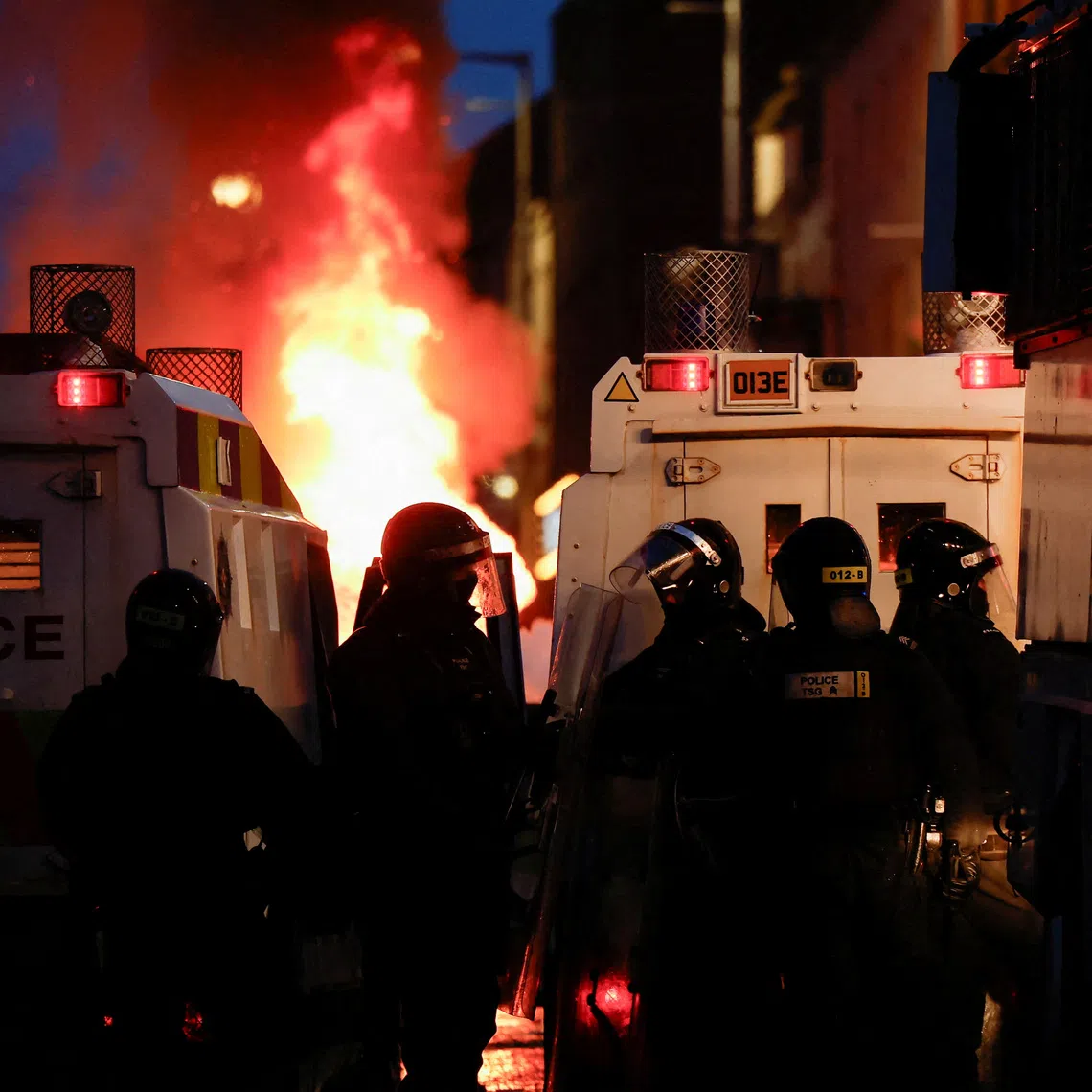 FILE PHOTO: Police officers stand guard behind police vehicles as flames rise during a the second night of riots, in Ballymena, Northern Ireland, June 10, 2025. REUTERS/Clodagh Kilcoyne/File Photo