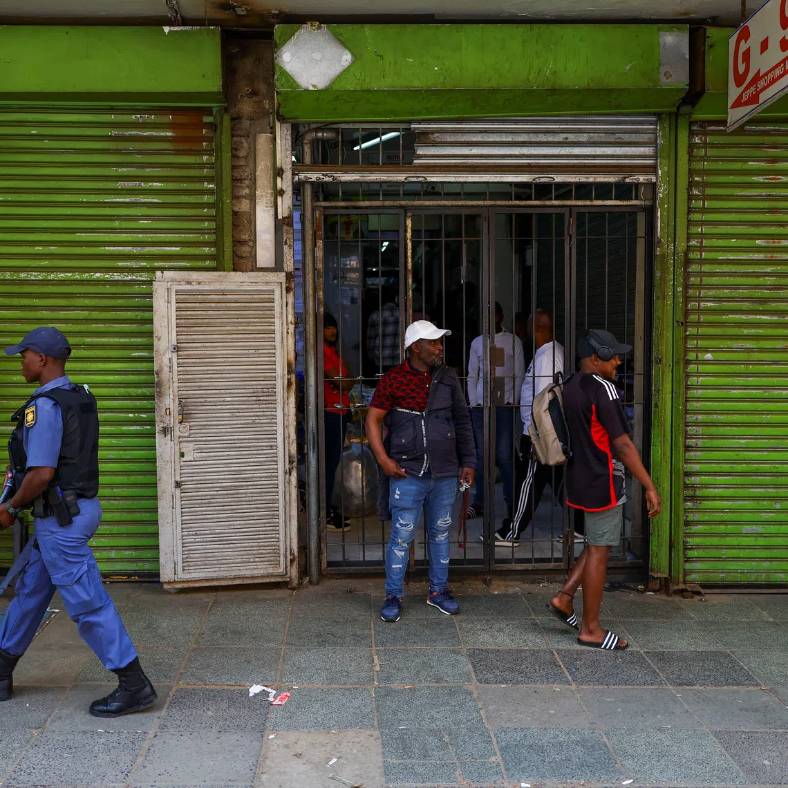 A police officer carrying a weapon walks past a shop as police maintain a presence during a march following anti-migrant unrest in Johannesburg and the coastal city of Durban, where vehicles were torched and foreign-owned shops were looted, in Johannesburg, South Africa, October 9, 2026. REUTERS/Siphiwe Sibeko