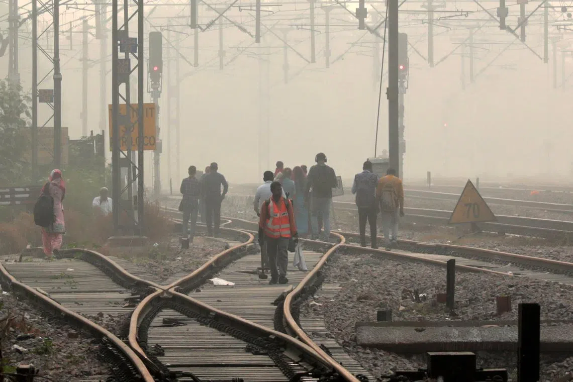 Commuters walk on a railway track as a thick layer of smog engulfs the city in New Delhi on Nov 5.