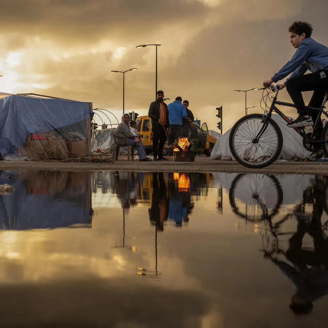 A family stand next to a fire outside their tent, at a temporary encampment for displaced people, amid escalating hostilities between Israel and Hezbollah, as the U.S.-Israel conflict with Iran continues, in Beirut, Lebanon, March 30, 2026. REUTERS/Adnan Abidi TPX IMAGES OF THE DAY