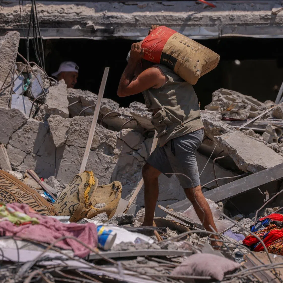 A Lebanese carries a bag of cement as he walks amid the rubble of a building destroyed in an Israeli airstrike, attempting to repair his home which was damaged in the strike in Tyre, Lebanon.