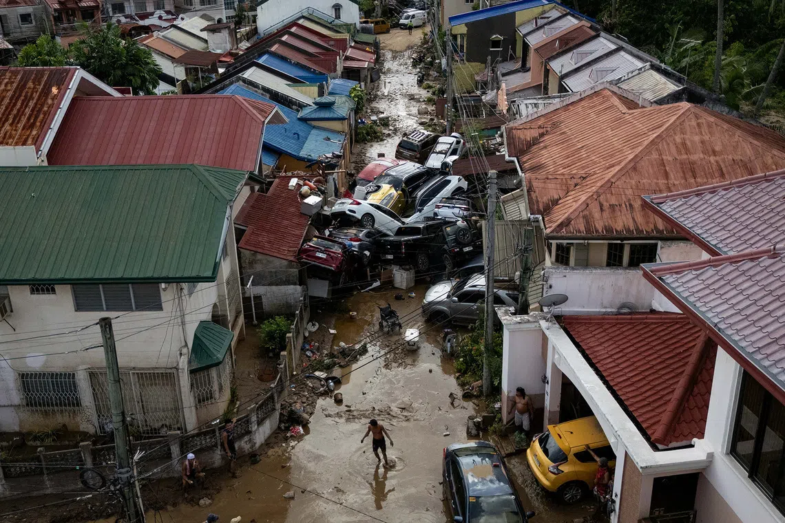 A man crosses a muddy street piled up with cars that were swept away in floods brought on by Typhoon Kalmaegi, in Bacayan, Cebu City, Philippines, on Nov 5, 2025. 