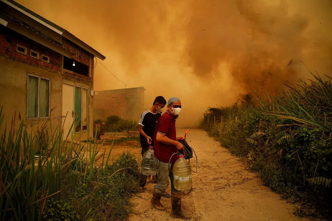 Residents carrying containers of water as a wildfire burns near a residential area in Banyuasin, South Sumatra province, Indonesia, on Oct 7.