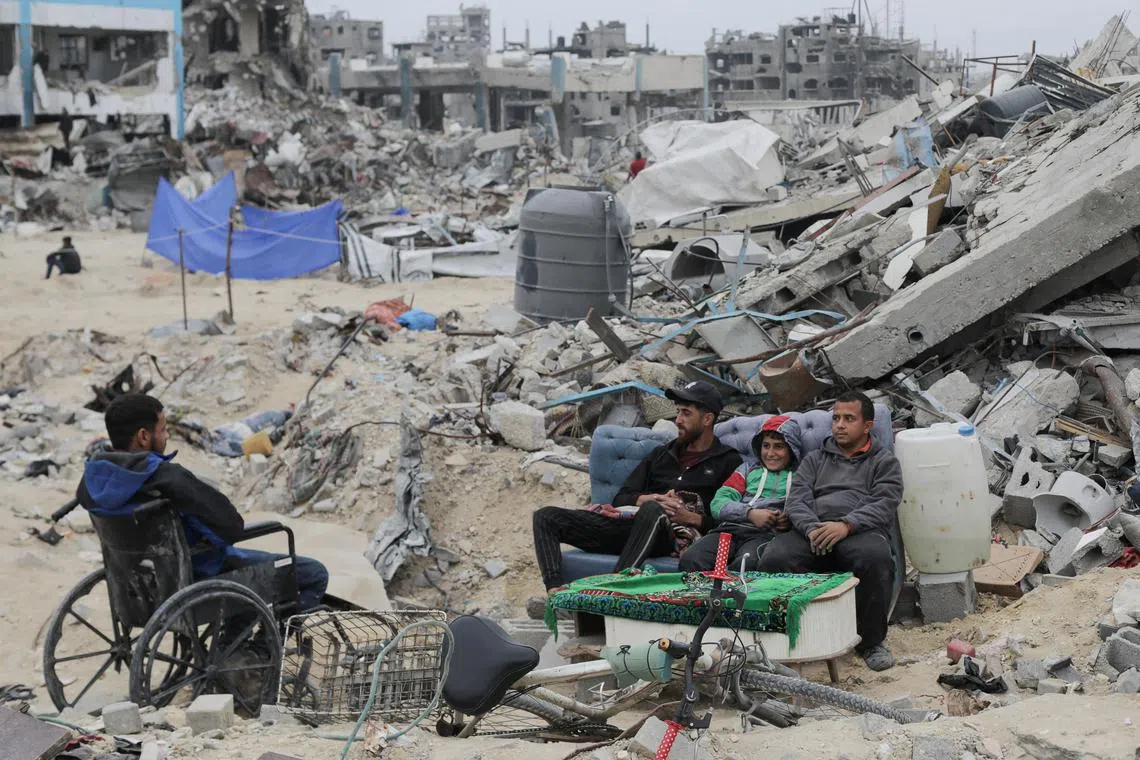 Palestinians sit next to rubble of a building destroyed during the Israeli offensive, amid a ceasefire between Israel and Hamas, in Jabalia in the northern Gaza Strip, January 22, 2025. REUTERS/Mahmoud Issa
