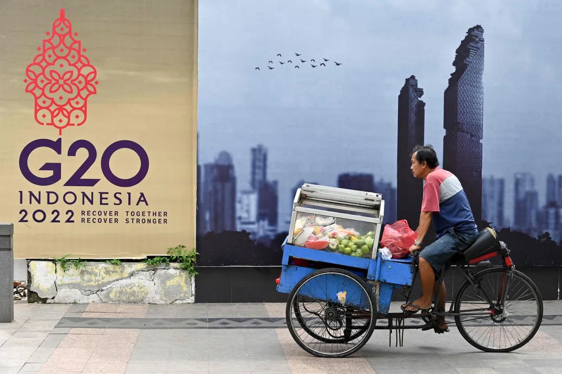 A fruit vendor rides his cart past a logo of the G-20 Summit in Jakarta. 