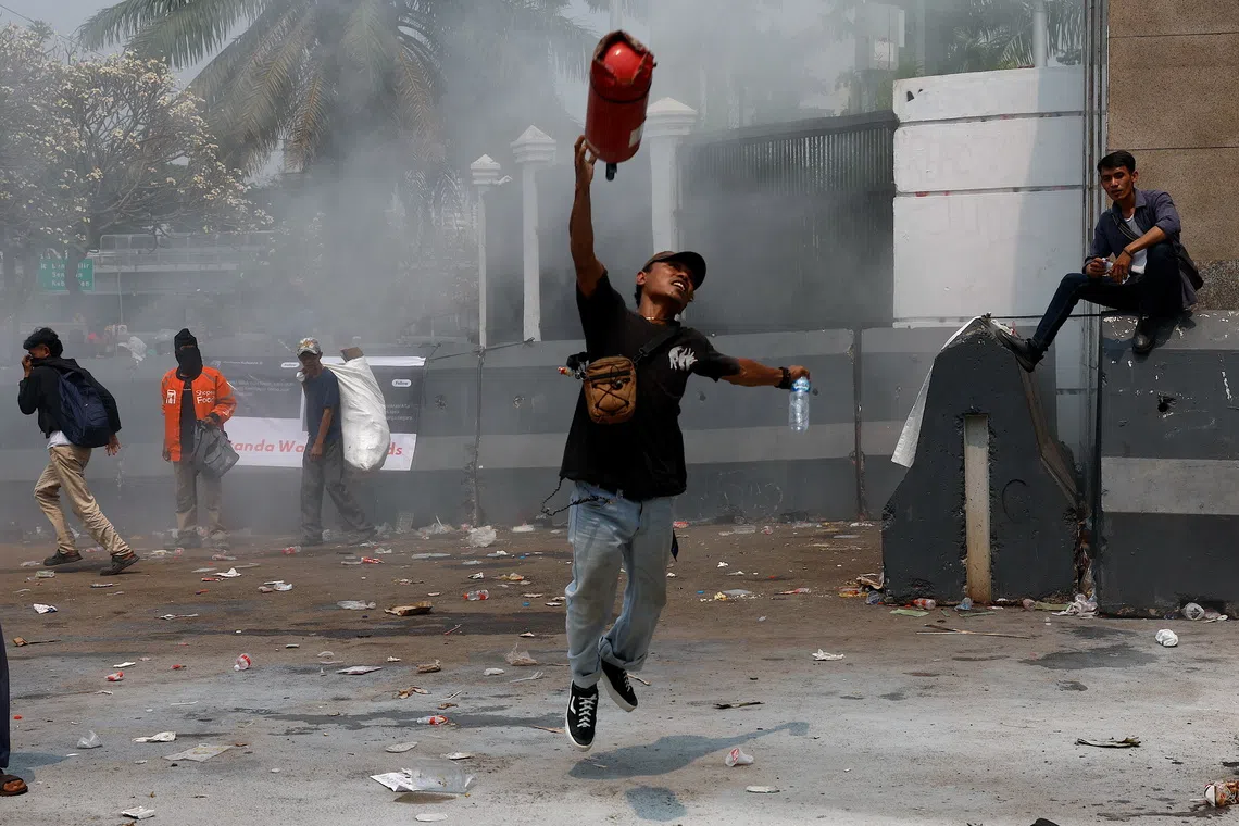 A protester throws an empty fire extinguisher canister during a protest against corruption outside the Parliament building in Jakarta.