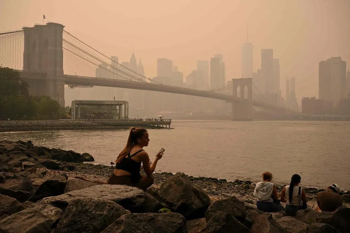 TOPSHOT - People sit near the Brooklyn Bridge as wildfire smoke from Canada causes hazy conditions on July 16, 2026 in New York. Out-of-control wildfires were raging Thursday in the Canadian province of Ontario, prompting evacuations and sending dangerous smoke billowing into the United States where millions of people were exposed to the unhealthy air. US states near the Canadian border including Minnesota, Wisconsin, Michigan and Illinois were particularly choked, as forecasters predicted the Northeast including New York would also see air quality continue to deteriorate. (Photo by ANGELA WEISS / AFP)