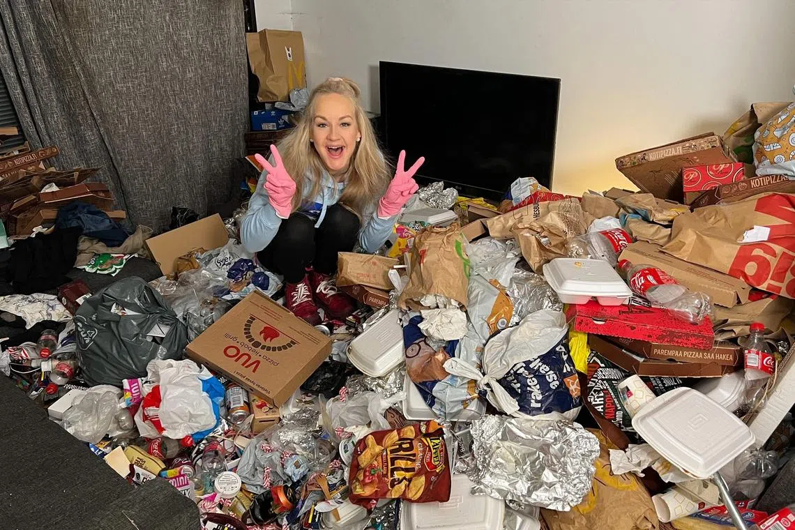 Finnish TikTok cleanfluencer Auri Kananen wearing pink gloves and making victory signs as she sits on a pile of trash and food remains in a flat in Helsinki, Finland.