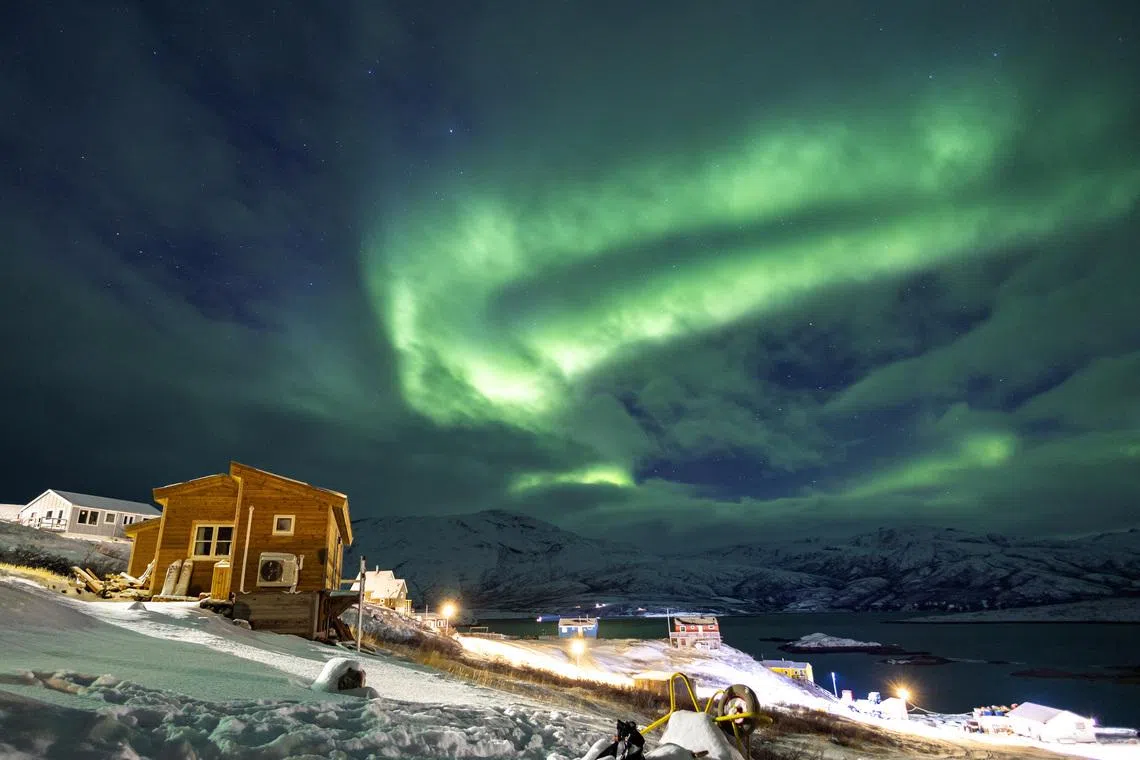 The Aurora Borealis, also known as the \"northern lights\", illuminates the sky over houses in Kapisillit, Greenland. REUTERS/Marko Djurica