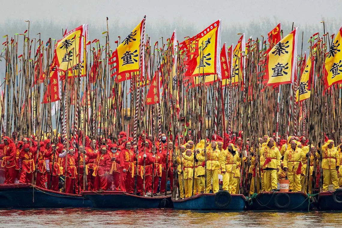 Participants standing with poles and flags on traditional boats during the Taizhou Jiangyan Qintong Boat Festival at the Qinhu National Wetland Park in Taizhou, in eastern China's Jiangsu province on April 6, 2024. 