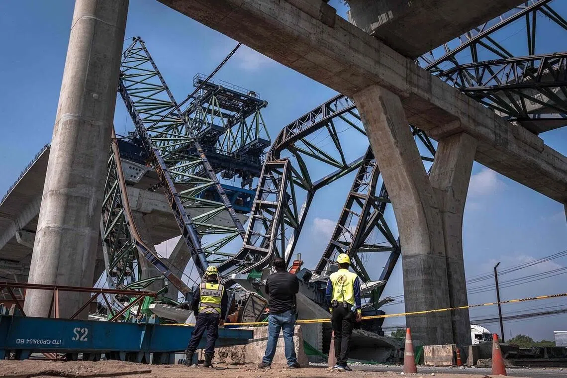TOPSHOT - Recovery workers stand at the site of a construction crane collapse onto a highway in Samut Sakhon on the outskirts of Bangkok on January 15, 2026. A crane at a highway construction site in the Bangkok suburbs collapsed on January 15, killing two people, a local police chief told AFP, one day after a crane fell on a train in Thailand, killing 32. (Photo by Chanakarn Laosarakham / AFP)
