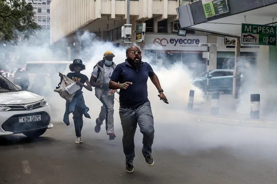 People running to take cover after tear gas is fired by Kenyan police officers during a demonstration against tax hikes as Members of the Parliament debate the Finance Bill 2024, in downtown Nairobi, on June 18, 2024. 