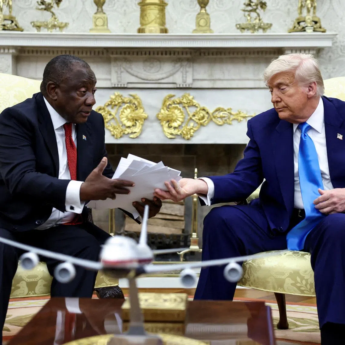 U.S. President Donald Trump hands over to South African President Cyril Ramaphosa copies of articles that he said showed white South Africans who had been killed, in the Oval Office of the White House in Washington, D.C., U.S., May 21, 2025. REUTERS/Kevin Lamarque