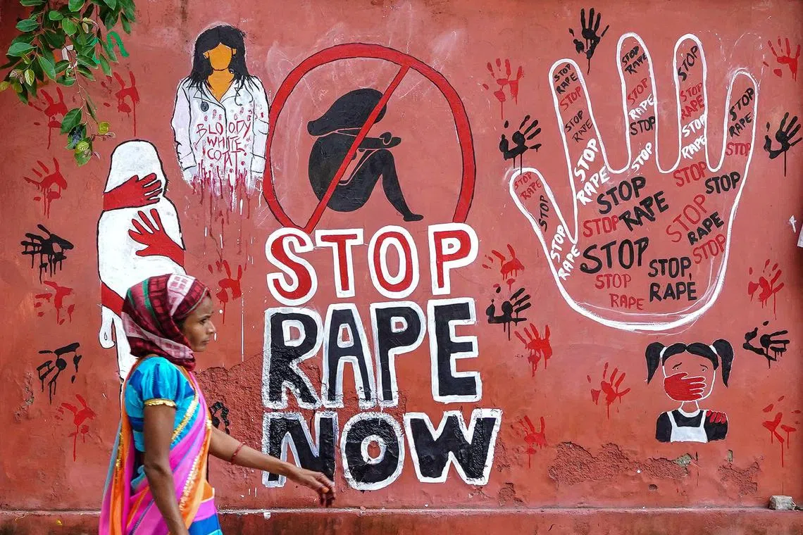 A woman walks past a mural painted on a roadside wall in Ajmer on August 17, 2024, condemning the rape and murder of a doctor in India's West Bengal state. Earlier this month, in a government-run hospital in the eastern city of Kolkata, the battered and bloodied body of a 31-year-old doctor was found, sparking outrage. The brutal attack has focused anger at the lack of measures in place for female doctors to do their job without fear, triggering protests and medical strikes. (Photo by Himanshu SHARMA / AFP) / TO GO WITH India-doctors-strike-women, FOCUS by Aishwarya KUMAR
