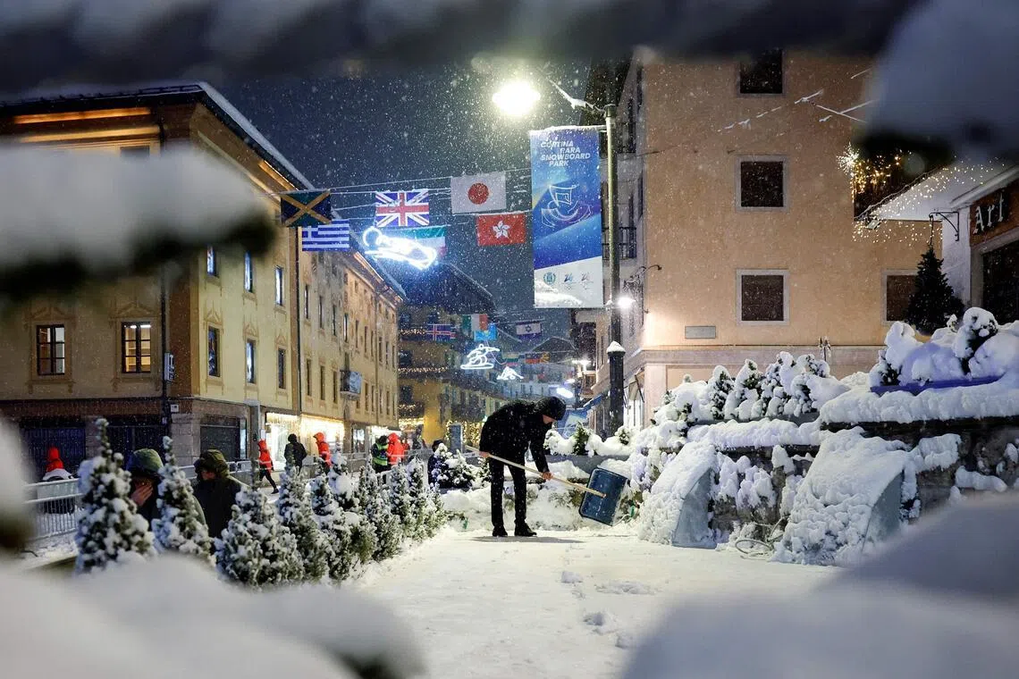 A business manager shovels snow outside a restaurant during snowfall in the main shopping area in Cortina d'Ampezzo.
