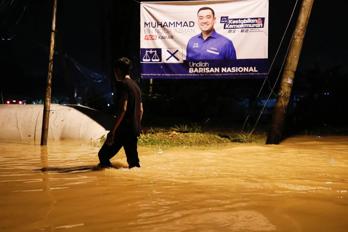 A man passes through a flooded area next to an election campaign banner during a flash flood in Klang, Selangor, Malaysia on Nov 10, 2022. 