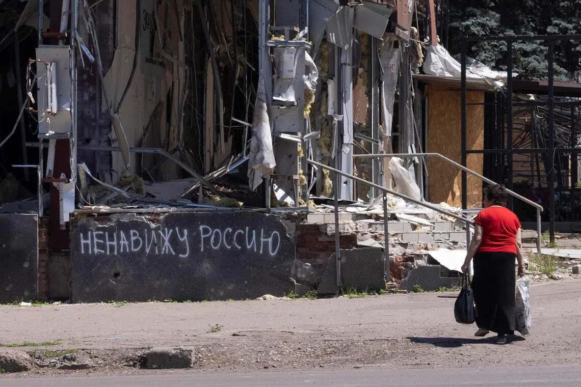 A resident of Kramatorsk, in eastern Ukraine, walks past a building destroyed by a Russian air strike with writing on the wall that reads "I hate Russia", on June 8.
