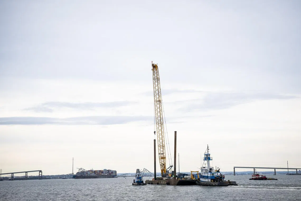 A crane on a barge is pushed toward the collapsed Francis Scott Key Bridge.