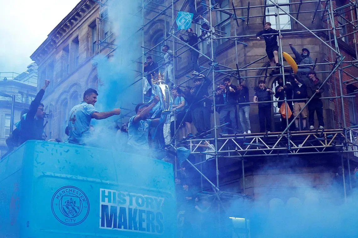 Manchester City's Ruben Dias holding the Premier League trophy as Rodri and Matheus Nunes celebrate on the bus during the victory parade on May 26.