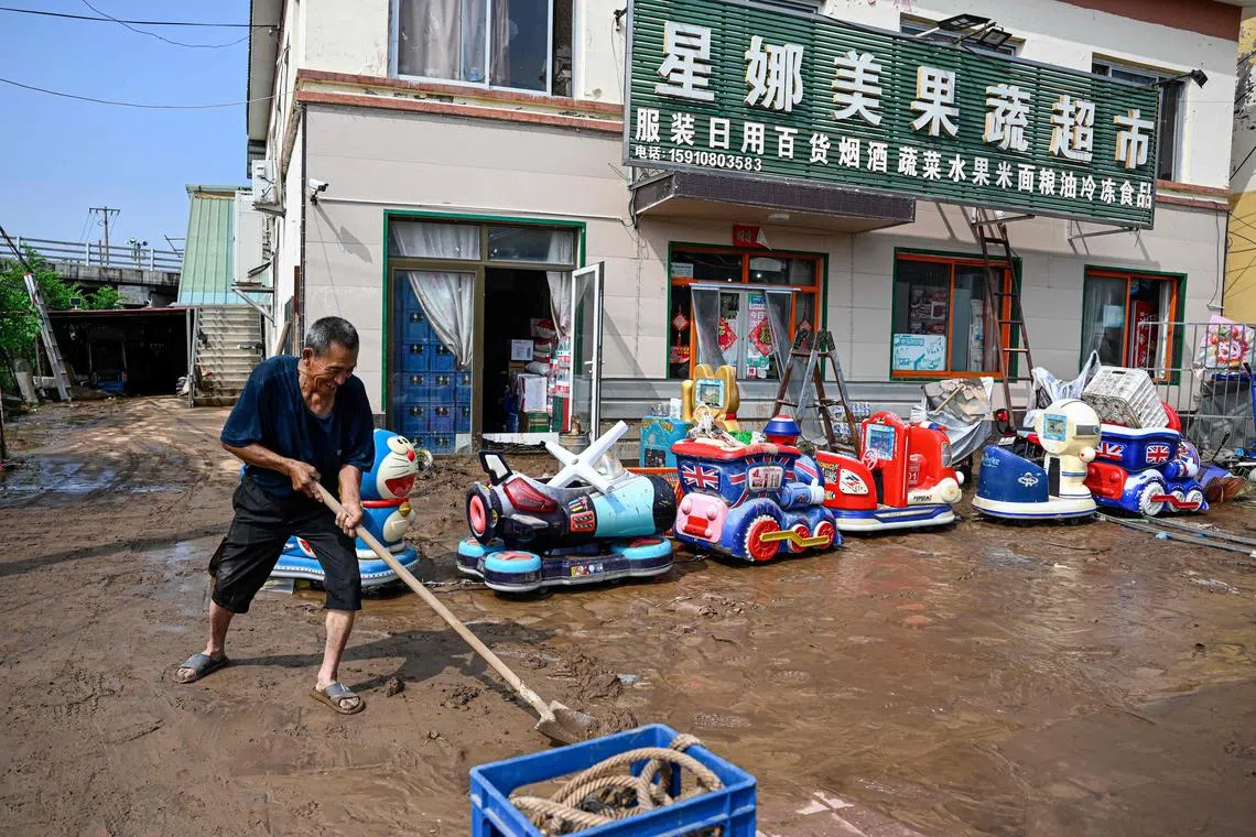 TOPSHOT - An elderly man clears mud in front of a flooded market after heavy rains at Taishitun village in Miyun district, on the outskirts of Beijing on July 28, 2025. Torrential rain soaking northern China triggered a deadly landslide, burst riverbanks and washed away cars on July 28, with thousands of people forced to evacuate the days-long deluge. (Photo by Jade GAO / AFP)