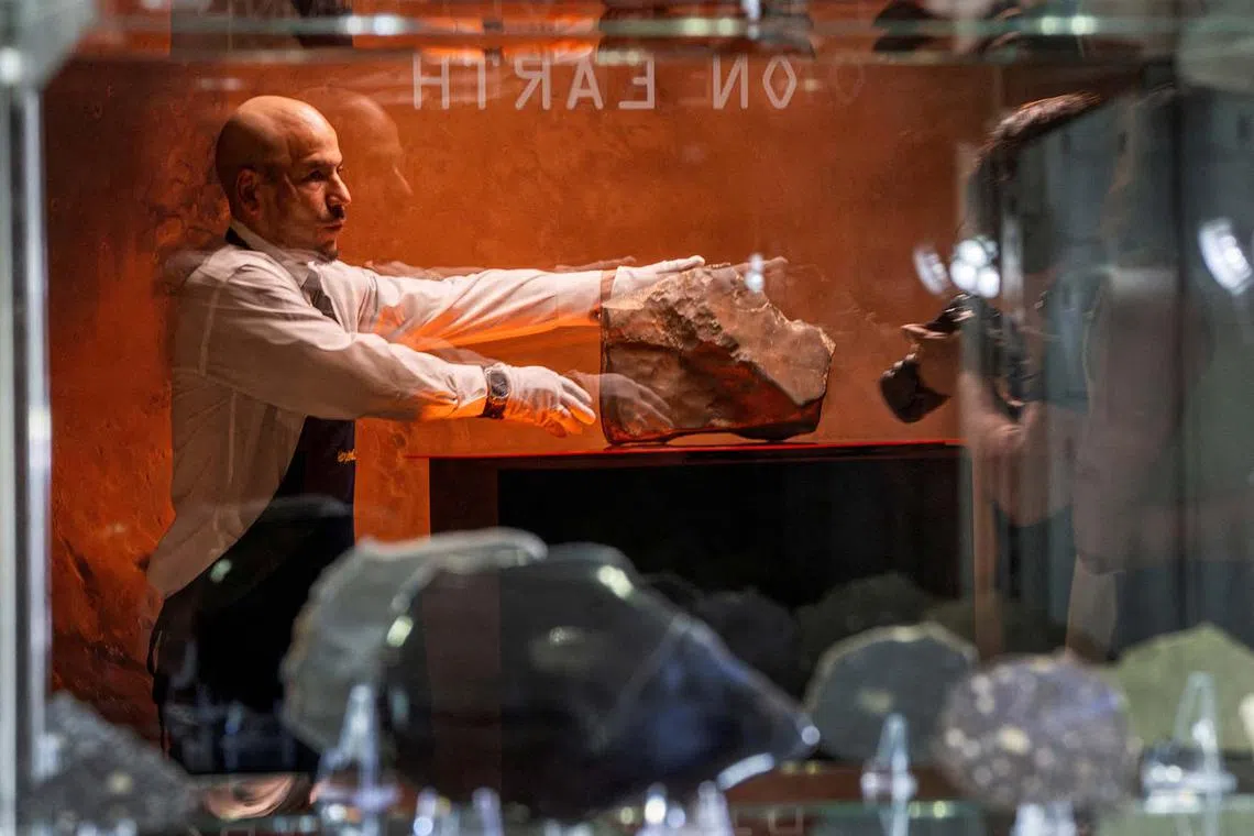 A handler is reflected on a showcase as he organizes meteorite NWA 16788, the largest known piece of Mars on Earth, during the press preview of Sotheby’s Natural History auction in New York City on July 8. 