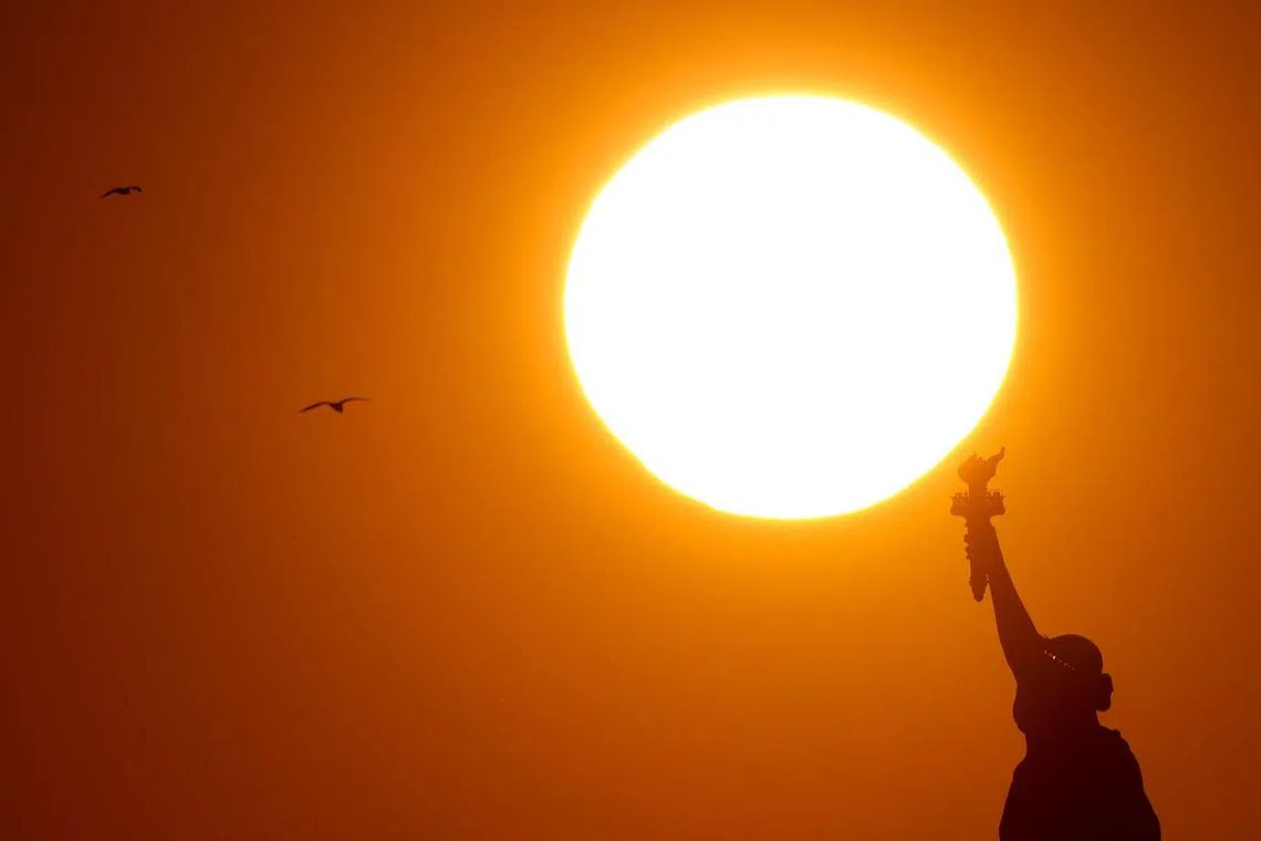 The sun setting behind the Statue of Liberty in New York City on Dec 13, 2023. 