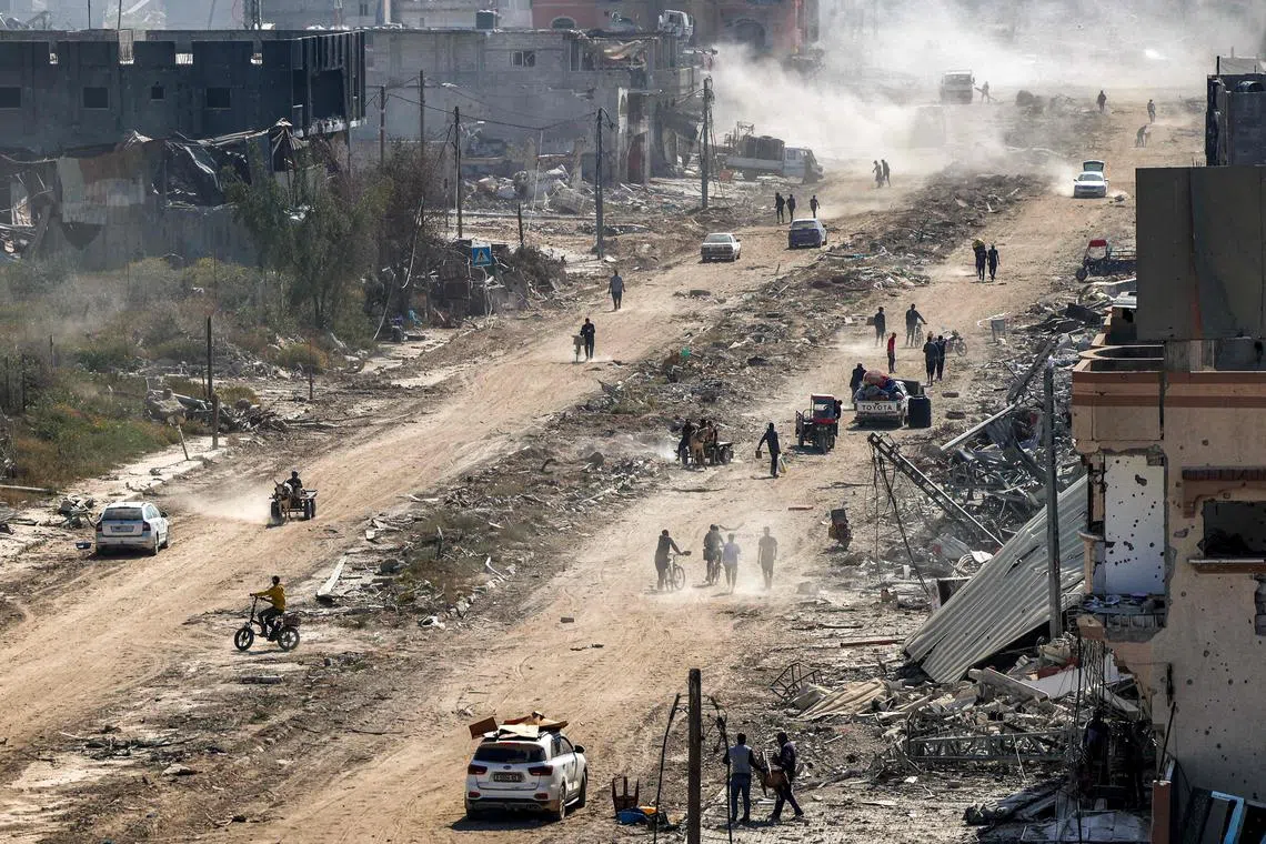 People walk past destroyed buildings along a road in Khan Yunis, on April 7, after Israel pulled its ground forces out of the southern Gaza Strip.