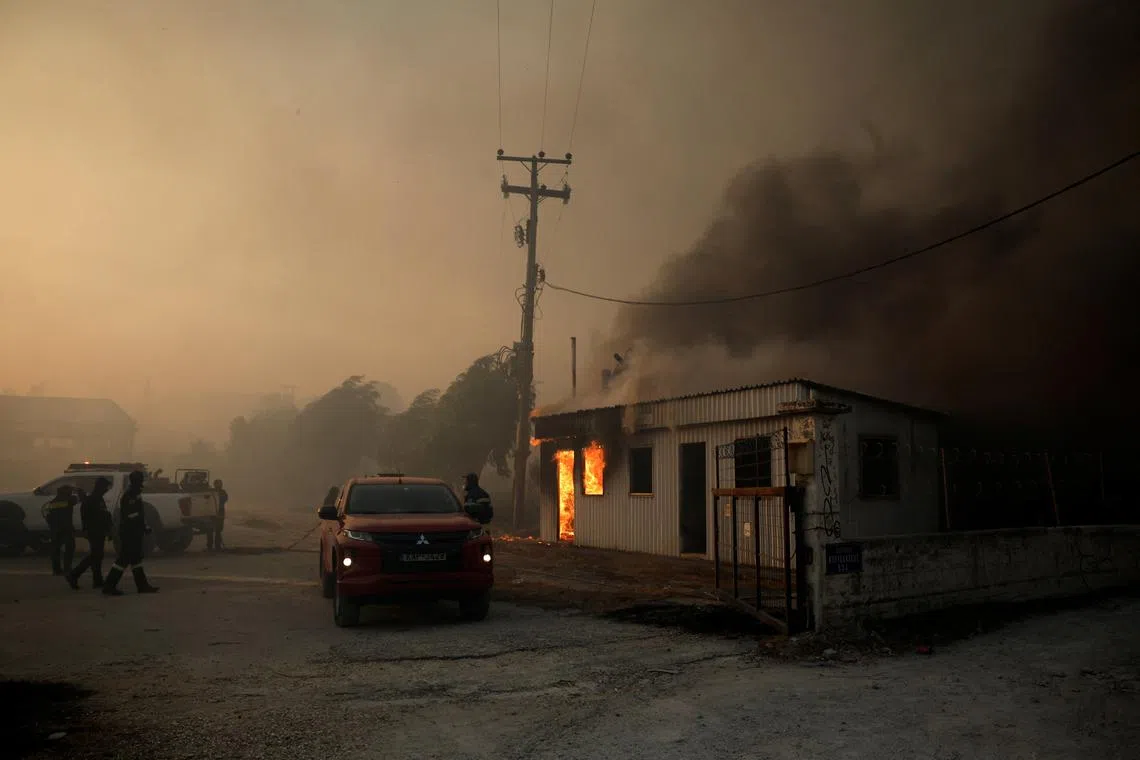 Firefighters work to extinguish a fire from a building during a wildfire, in Sichaina near Patras, Greece, on Aug 13.