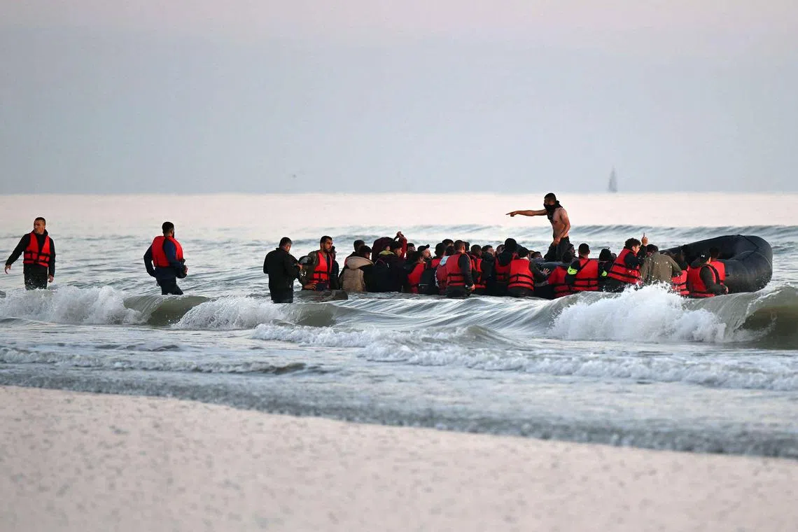 A 2022 photo shows a smuggler (centre) stands among 40 or so migrants boarding an inflatable boat before they attempt to cross the English Channel illegally, from France to Britain.