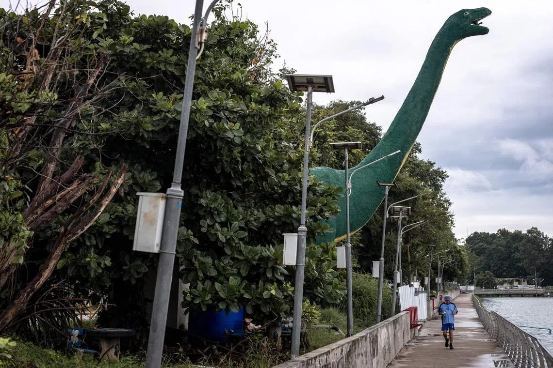 TOPSHOT - A man jogs past a dinosaur statue at Bueng Kaen Nakhon Public Park in Khon Kaen on August 20, 2026. (Photo by Chanakarn LAOSARAKHAM / AFP)