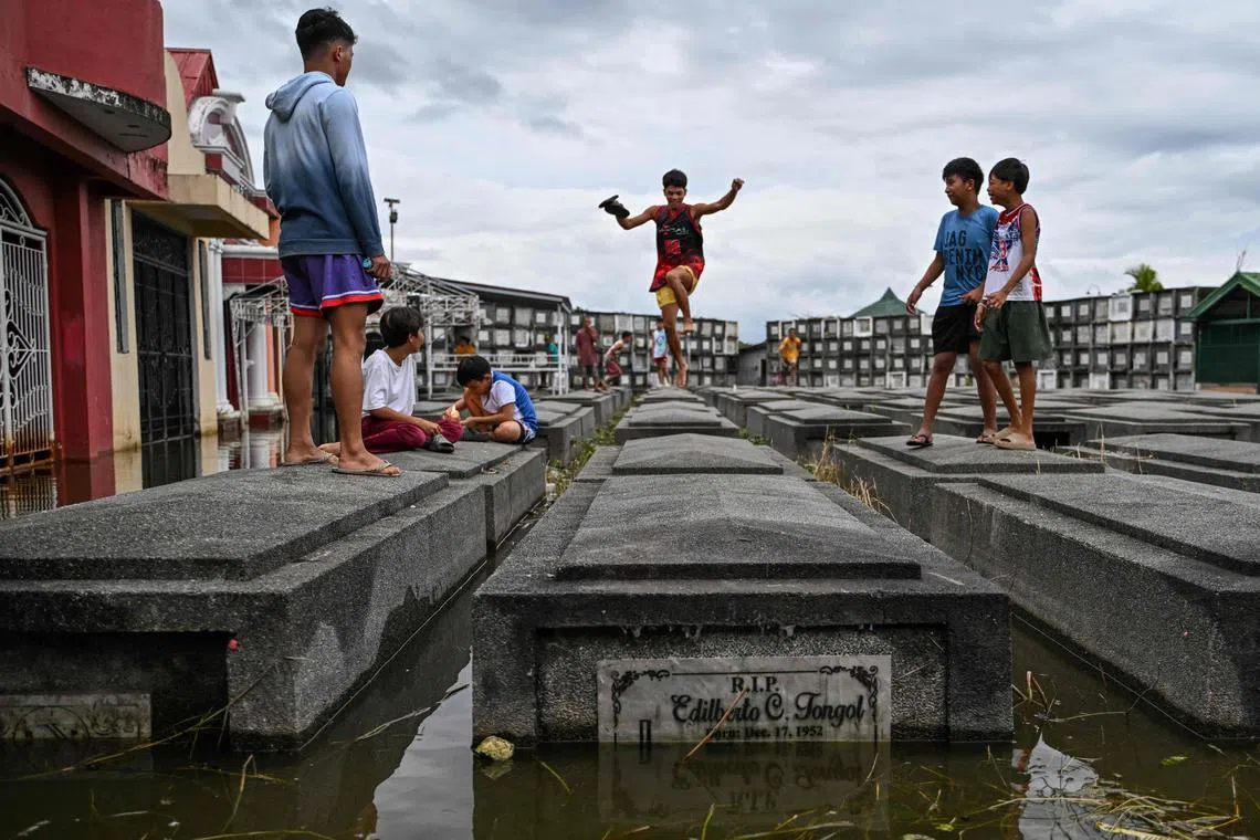 Boys jumping on tombs as they visit a submerged cemetery in Masantol, Pampanga provence, Philippines, on October 31, 2024.