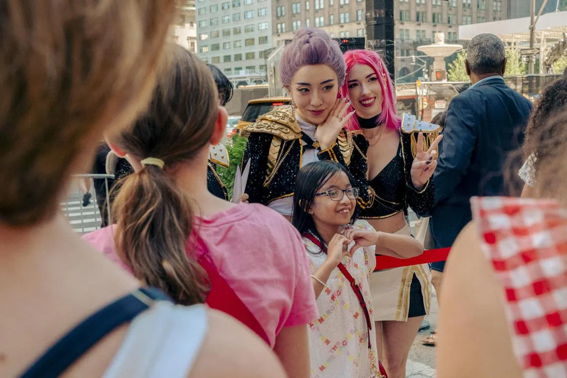 A fan poses with actors dressed as members of Huntrix, the group featured in the animated film “KPop Demon Hunters,” at a singalong screening of the film at Paris Theater in New York, Aug. 23, 2025. Kids and their parents celebrated their fandom at a singalong showing of “KPop Demon Hunters.” (Ye Fan/The New York Times)
