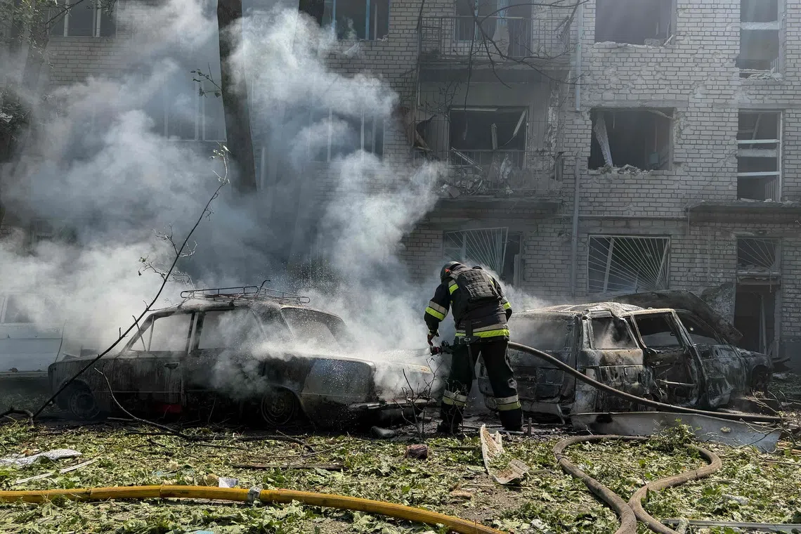 TOPSHOT - A Ukrainian firefighter puts off the fire in a car next to a damaged residential building at the site of a Russian airstrike in Zaporizhzhia on August 10, 2026, amid the Russian invasion of Ukraine. (Photo by Darya NAZAROVA / AFP)