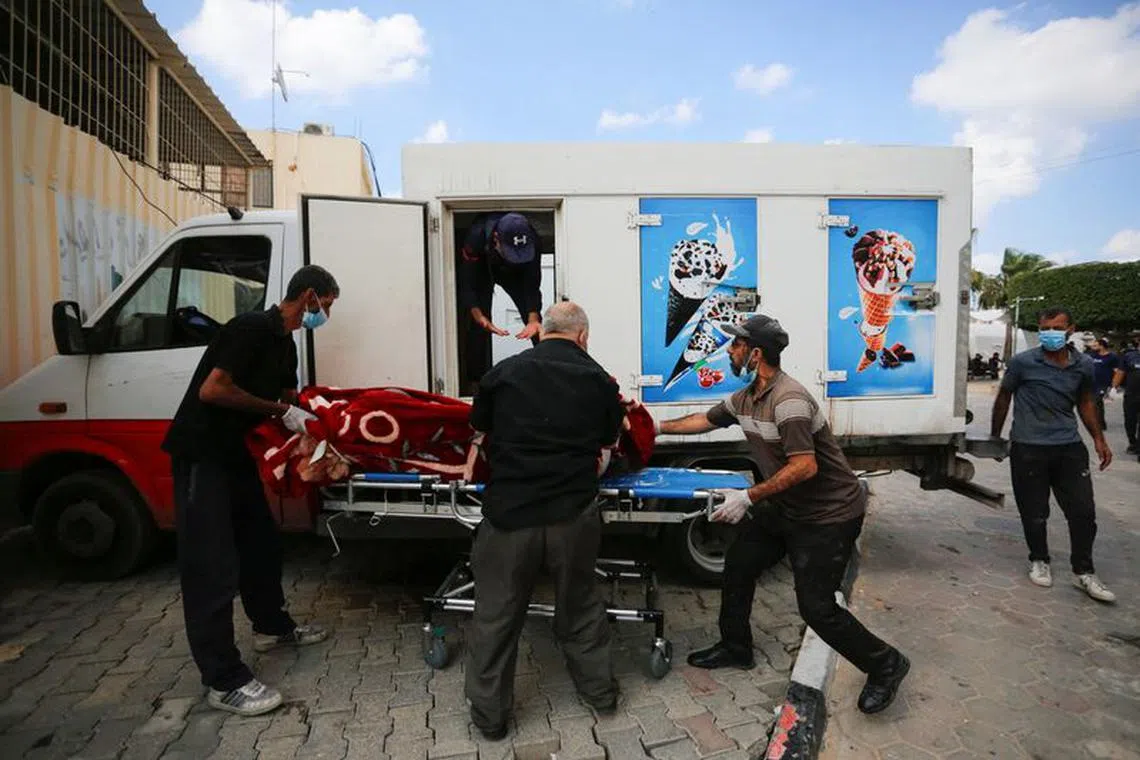 People carry the body of a Palestinian, who was killed in Israeli strikes, from an ice cream truck where it was kept, as the hospital morgues are packed, amid the ongoing Israeli-Palestinian conflict, in the central Gaza Strip October 15, 2023. REUTERS/Stringer