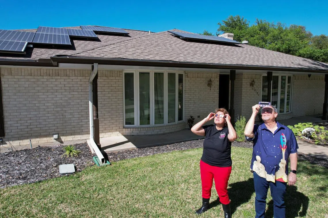 Eclipse chaser Leticia Ferrer and her husband Daniel Brookshier observe the sun through eclipse glasses, in front of their home in Dallas, Texas, U.S., April 3, 2024. REUTERS/Evan Garcia