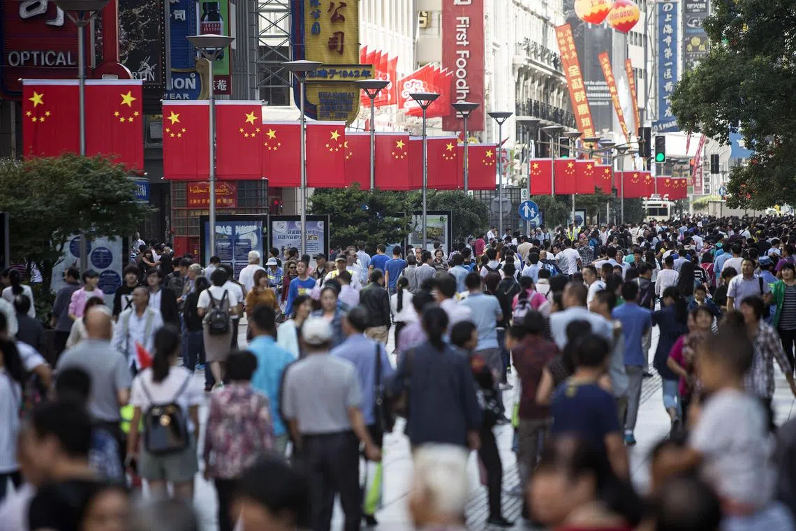 Pedestrians walk past Chinese national flags displayed along the Nanjing Road pedestrian street in Shanghai, China, on Friday, Oct. 2, 2015. China's consumer inflation moderated and factory gate deflation extended a record stretch of declines, signaling the People's Bank of China still has room to ease monetary policy further to support a slowing economy. Photographer: Qilai Shen/Bloomberg