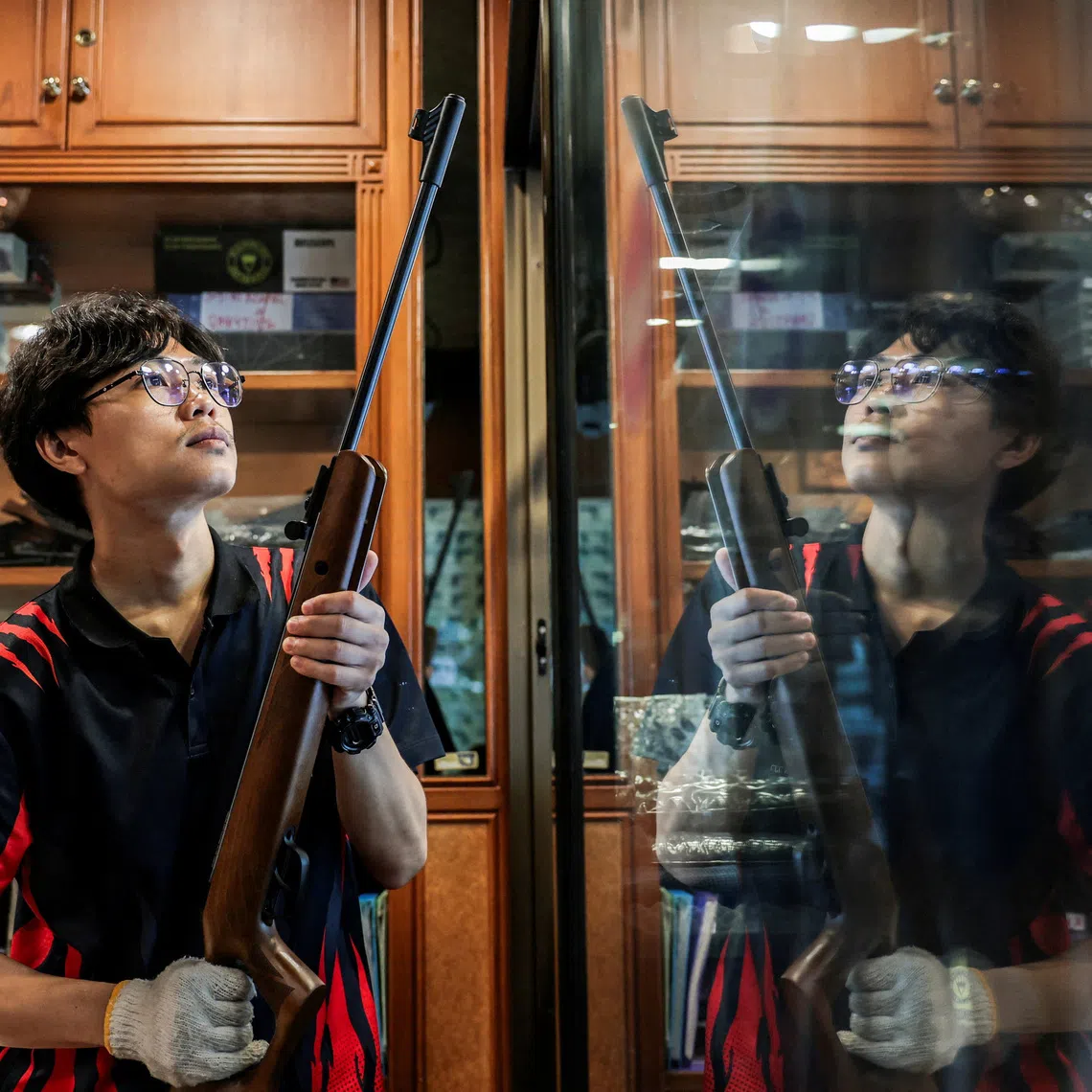 A worker at a gun shop places a firearm back among others on a display shelf after cleaning.