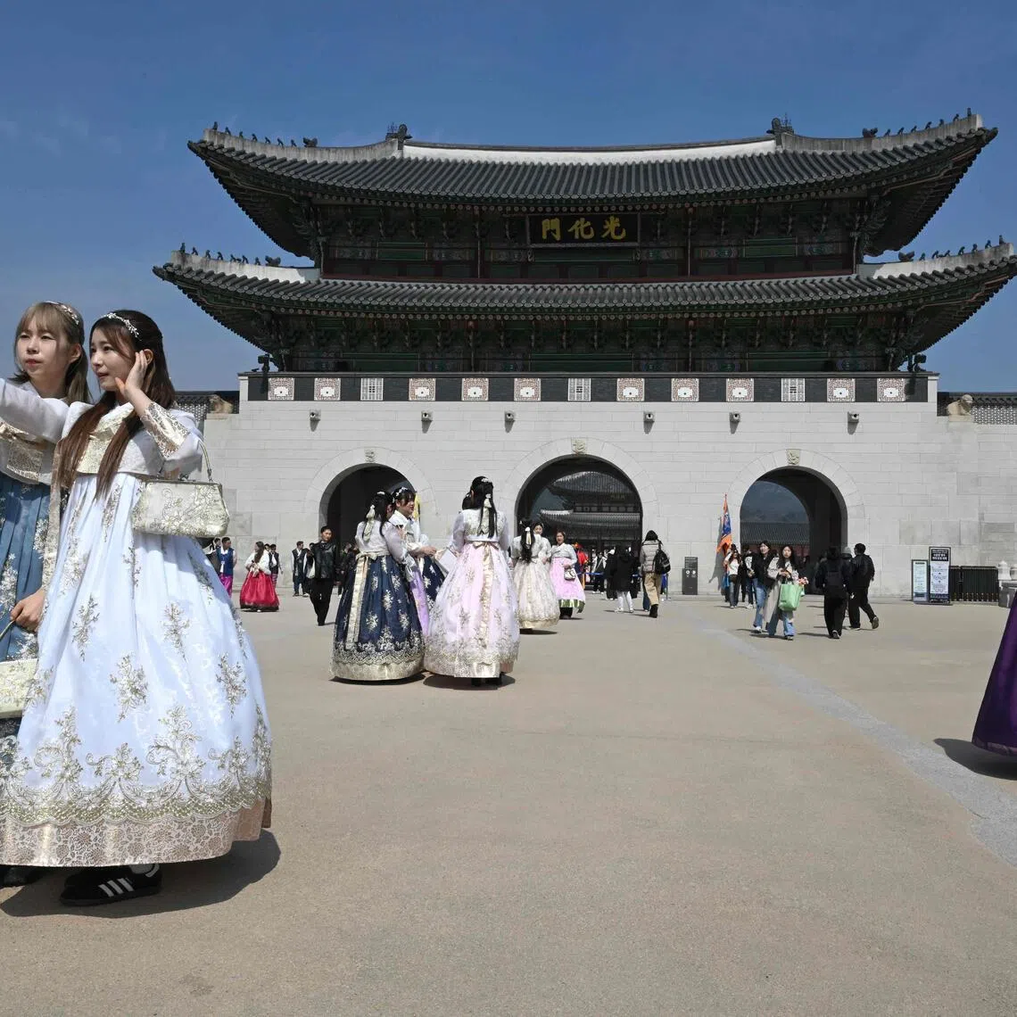This picture taken on March 16, 2026 shows visitors wearing traditional hanbok dresses taking a selfie in front Gwanghwamun Gate, the main gate of Gyeongbokgung Palace, in Seoul. The world's biggest boy band is set for a comeback concert on March 21, after a nearly four-year hiatus for the septet to do military service -- and while the nation went through traumatic times. (Photo by Jung Yeon-je / AFP) / TO GO WITH AFP STORY, SKorea-entertainment-music-BTS-politics,  FOCUS by Claire LEE
