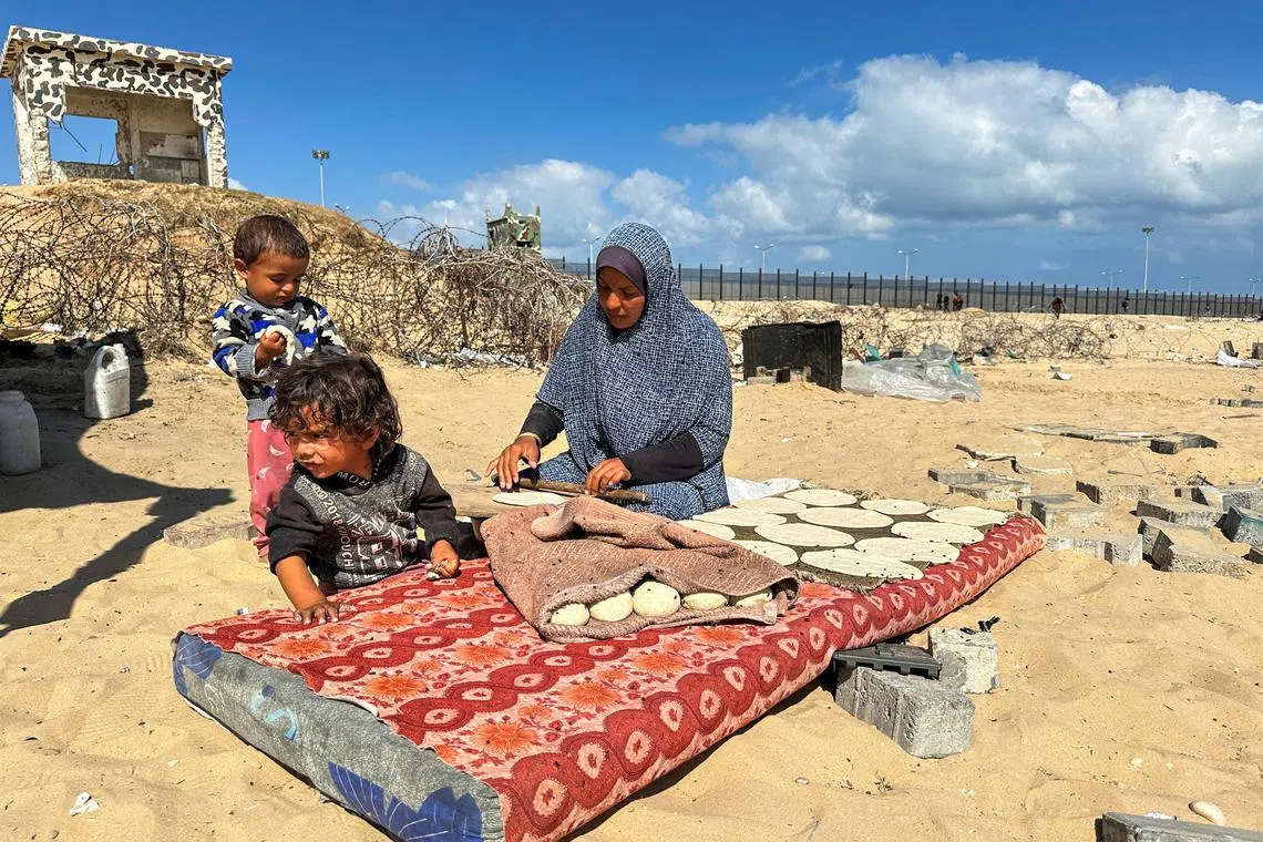 FILE PHOTO: A woman prepares food next to children, as displaced Palestinians take shelter at the border with Egypt, during an Israeli military operation, in Rafah in the southern Gaza Strip, May 29, 2024. REUTERS/Doaa Rouqa/File Photo