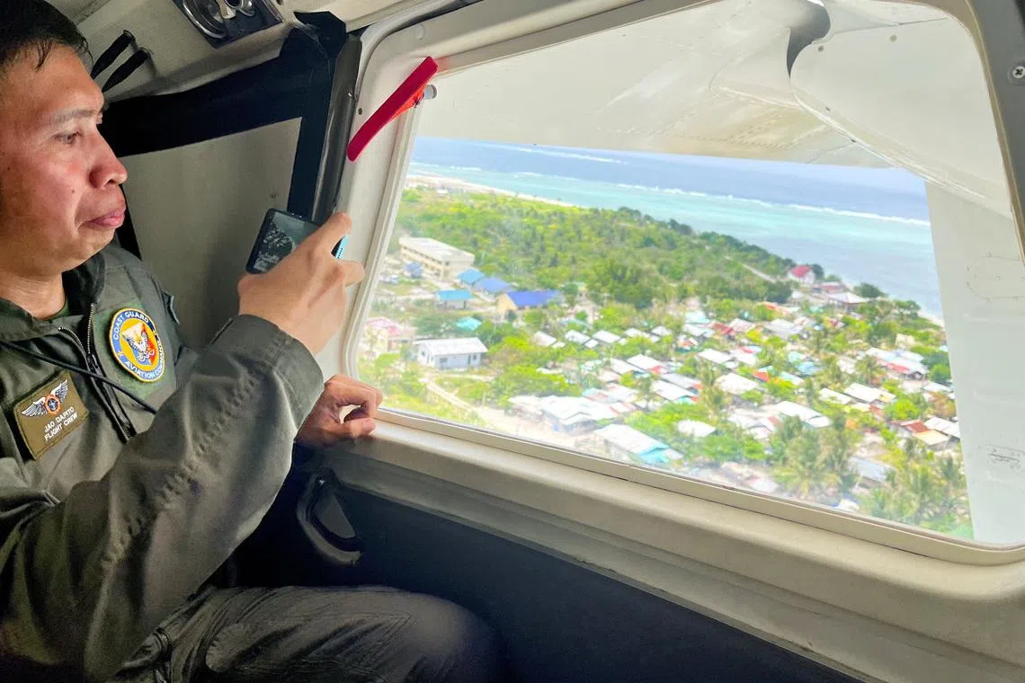 A Philippine Coast Guard member uses his phone to record the view of Philippine-occupied Thitu Island while onboard a plane in the disputed South China Sea, February 21, 2026. Picture taken with a mobile phone. REUTERS/Karen Lema
