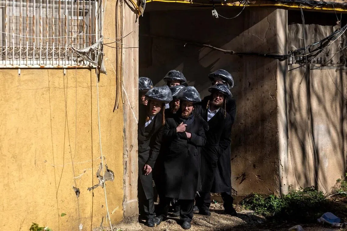 Ultra-Orthodox Jewish men look on from behind a wall during a protest by ultra-Orthodox Jewish people against pressure to conscript them into Israel's military, near a military recruitment office in Jerusalem, January 4, 2026. REUTERS/Ronen Zvulun