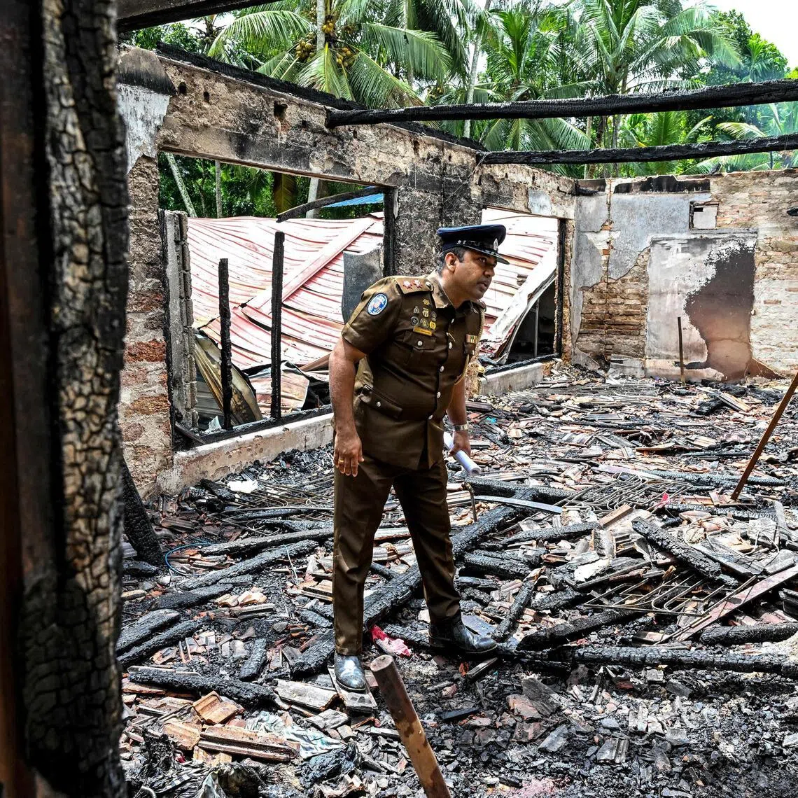 A policeman inspects a burnt elder care home in Sri Lanka's Batagoda, a day after a fire broke outand killed 12 residents.