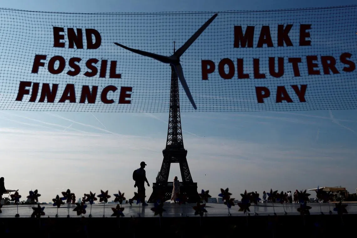 FILE PHOTO: Activists with Glasgow Actions Team and 350.org hold a floating \"invisible banner\" that will appear to transform the Eiffel Tower into a wind turbine to welcome world leaders on the eve of the Summit for a New Global Financial Pact, at the Trocadero Square in Paris, France, June 21, 2023. The slogan reads \"End Fossil Finance\" and \"Make Polluters Pay\". REUTERS/Gonzalo Fuentes/File Photo