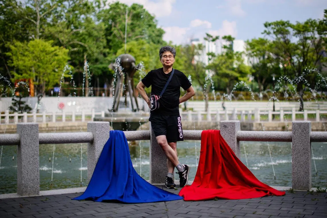 In this photo taken in Daegu, for decades synonymous with conservatism, on May 26, 2025, Kim Sung-gyun, 60, a former automotive industry worker, stands next to blue and red cloths to indicate he is undecided on whether he will be voting for Kim Moon-soo, the presidential candidate for the conservative People Power Party or Lee Jae-myung, the presidential candidate for the Democratic Party, in the upcoming presidential elections. Kim said he is undecided. He disagreed with Yoon's attempt to impose martial law, which he described as creating "extreme chaos". "People's lives are already difficult enough." But he expressed reservations about one side gaining unchecked power -- pointing to the opposition's near two-thirds majority in parliament. "Balance is important," he said. He said he plans to vote for whoever he believes "puts the people first", regardless of traditional regional loyalties. (Photo by ANTHONY WALLACE / AFP) / To go with 'SKOREA-VOTE-DEMOCRACY, PENPIX' by Hailey JO