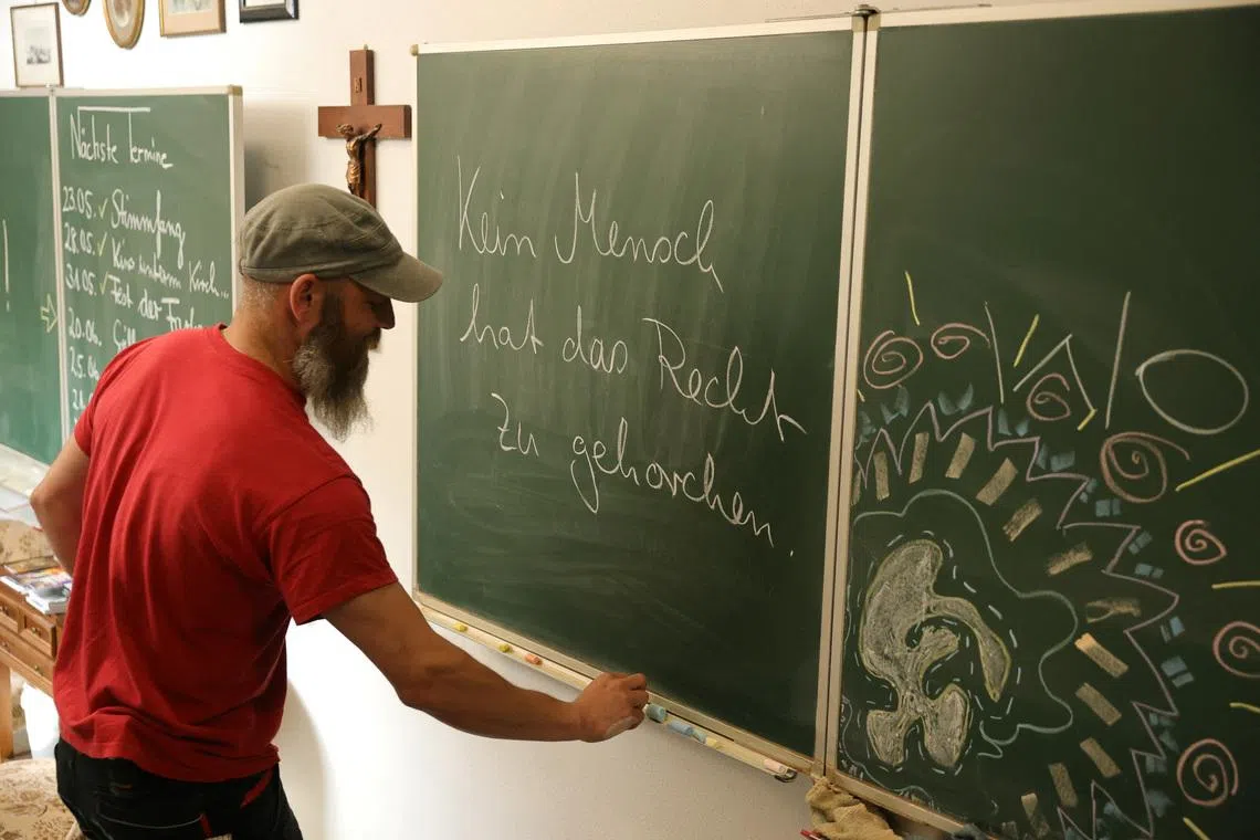 Max Heckel, a craft teacher at a secondary school who has been targeted by the local far-right Alternative for Germany (AfD) party over comments he made in class, writes on a board at his 'ANKER' event location in Arneburg, Germany, July 8, 2026. The words on the board reads \"No human being has the right to obey.\" REUTERS/Fabrizio Bensch