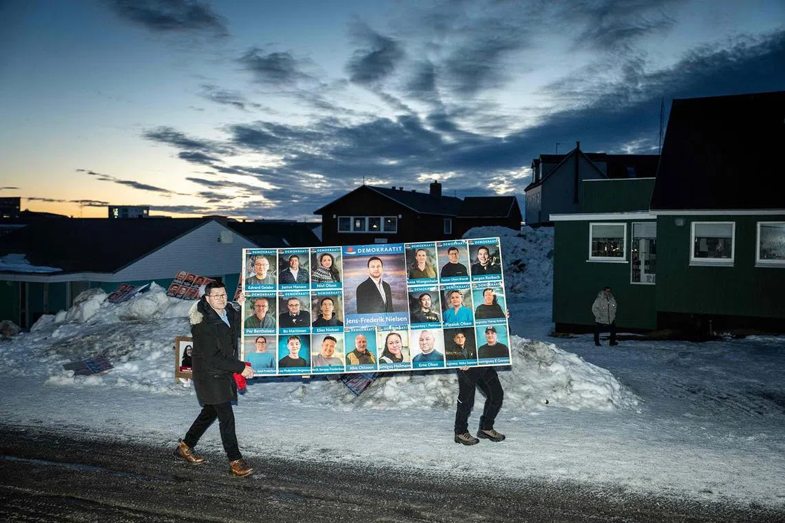 TOPSHOT - Men carry a large poster of the Democrats Party (Demokraatit) with a picture of party leader Jens-Frederik Nielsen (C) past a polling station during Greenland's legislative elections in Nuuk, Greenland, on March 11, 2025. The centre-right opposition Democrats have won a surprise victory in legislative elections in Greenland, the Danish territory coveted by US President Donald Trump, more than tripling their support to 29.9 percent of votes, official results showed on March 12. (Photo by Mads Claus Rasmussen / Ritzau Scanpix / AFP) / Denmark OUT
