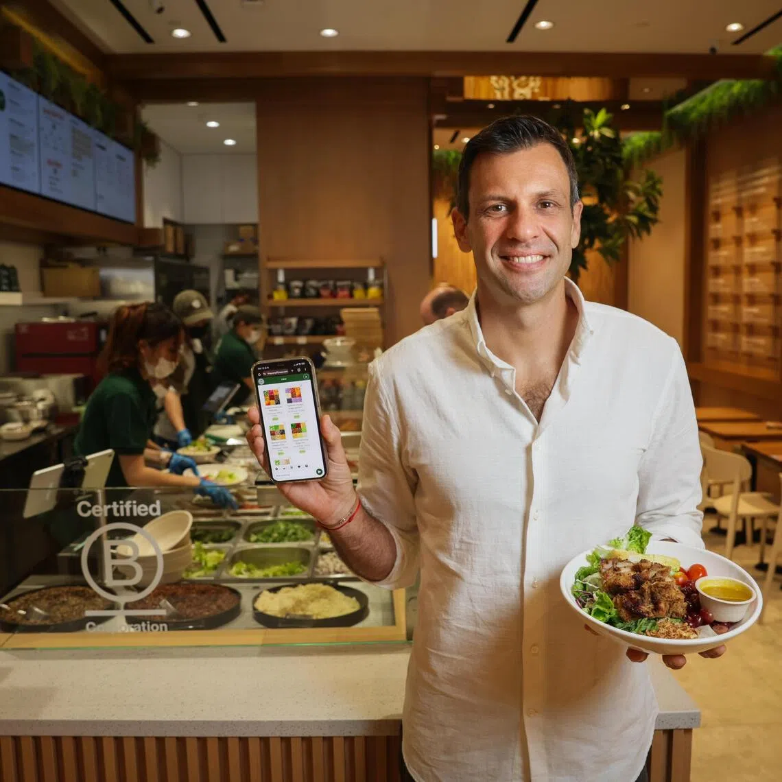Mr Adrien Desbaillets, the chief executive and co-founder of healthy food chain SaladStop! Group with Lulu, SaladStop!'s own GenAI assistant on his mobile phone and Lemongrass Chicken Bowl, which was recommended by Lulu.
